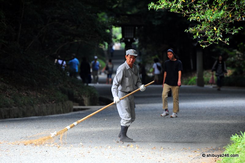 A workmen keeps the gravel paths clear from leaves
